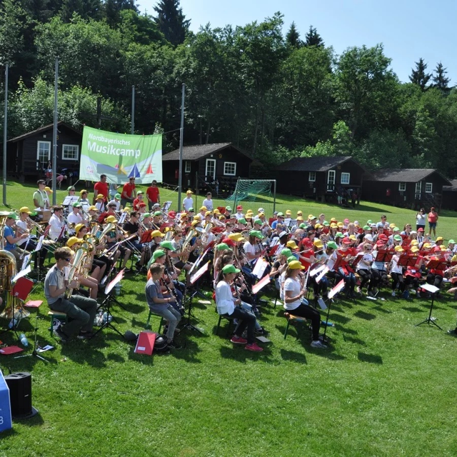 Viele Kinder und Jugendliche geben ein Konzert auf einer Wiese bei Sonnenschein. 