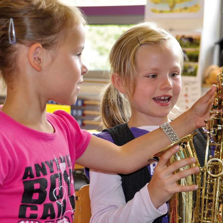 Zwei Mädchen betrachten fasziniert ein Saxophon. 