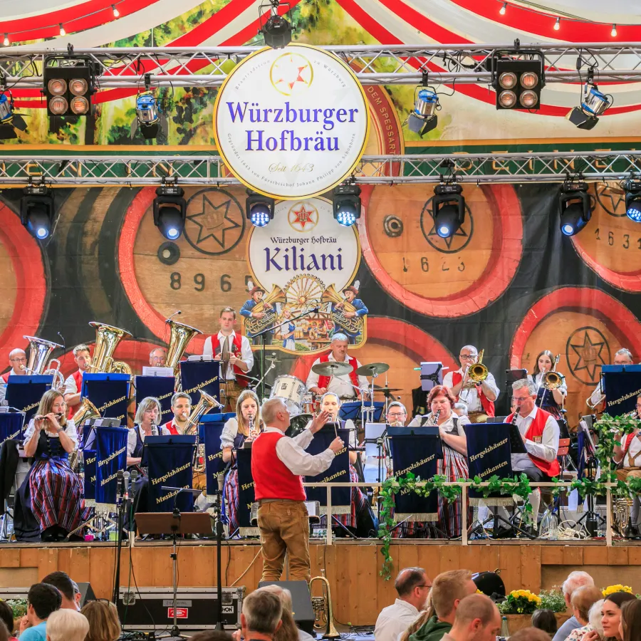 Eine Blaskapelle musiziert auf einer Festzelt-Bühne vor Publikum.