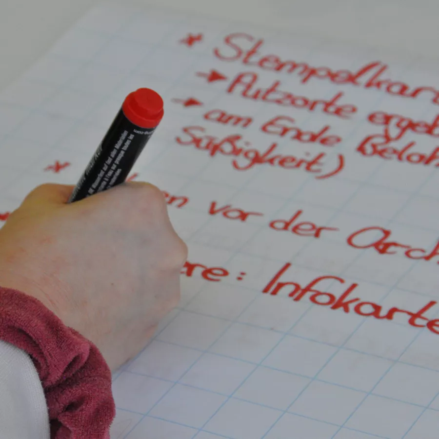 Nahaufnahme einer Hand mit Stift, die etwas auf ein großes Papier schreibt. 