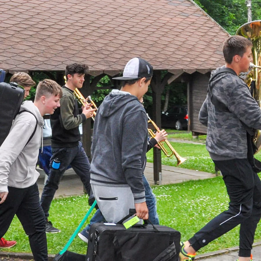 Mehrere Jungen laufen auf einem Weg mit Koffern und Instrumenten. 