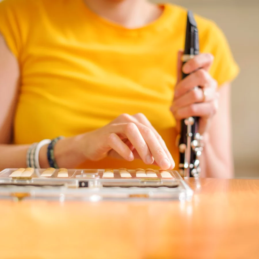 Eine Frau sitzt an einem Tisch und hält eine Klarinette in der Hand. Vor ihr auf dem Tisch liegen einige Klarinettenblätter. 