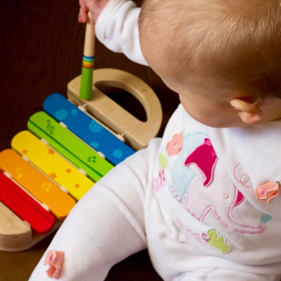 Ein Baby sitzt neben einem bunten Kinder-Glockenspiel und spielt darauf. 
