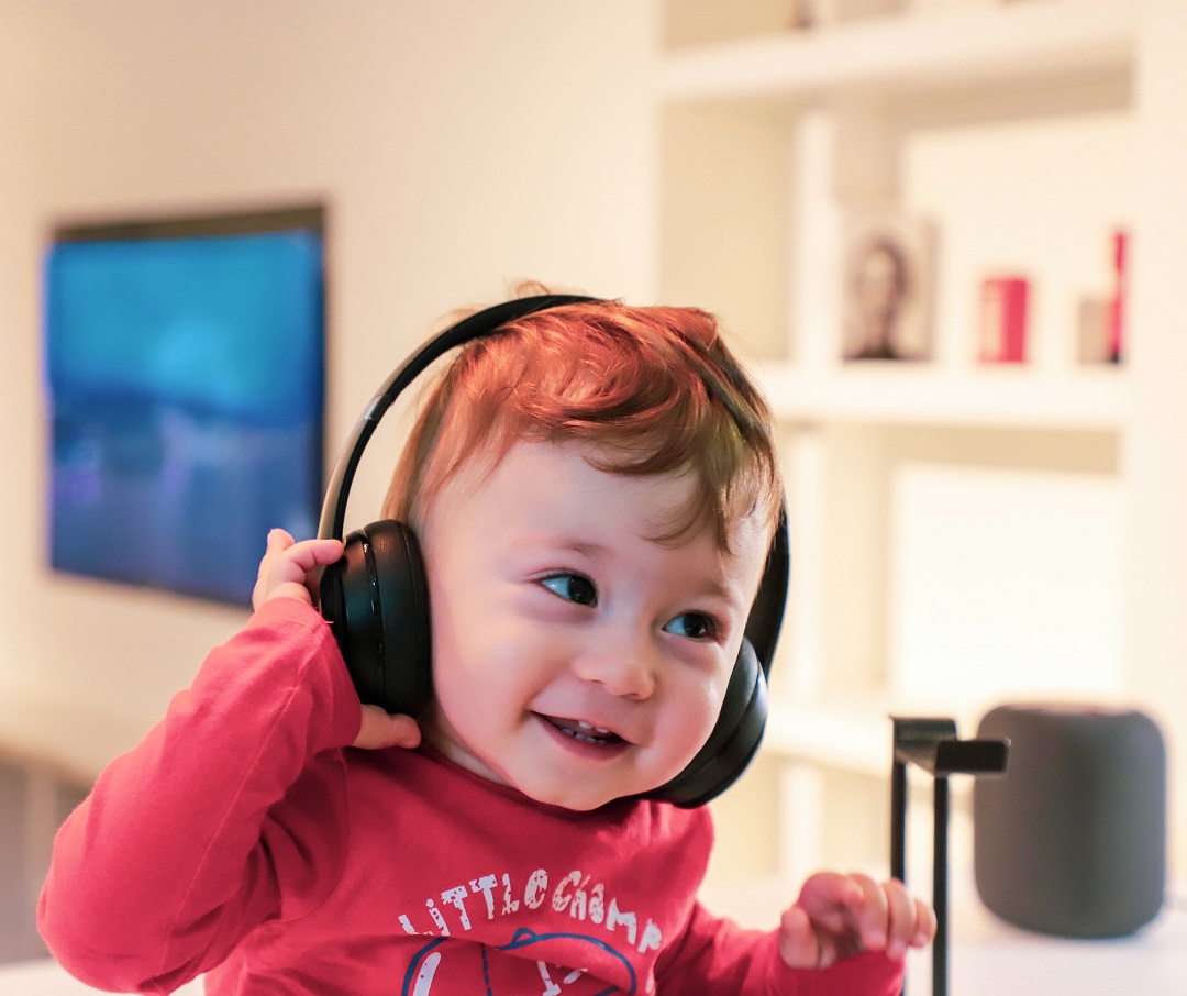 Ein Kleinkind hört mit Kopfhörern Musik und lacht. 