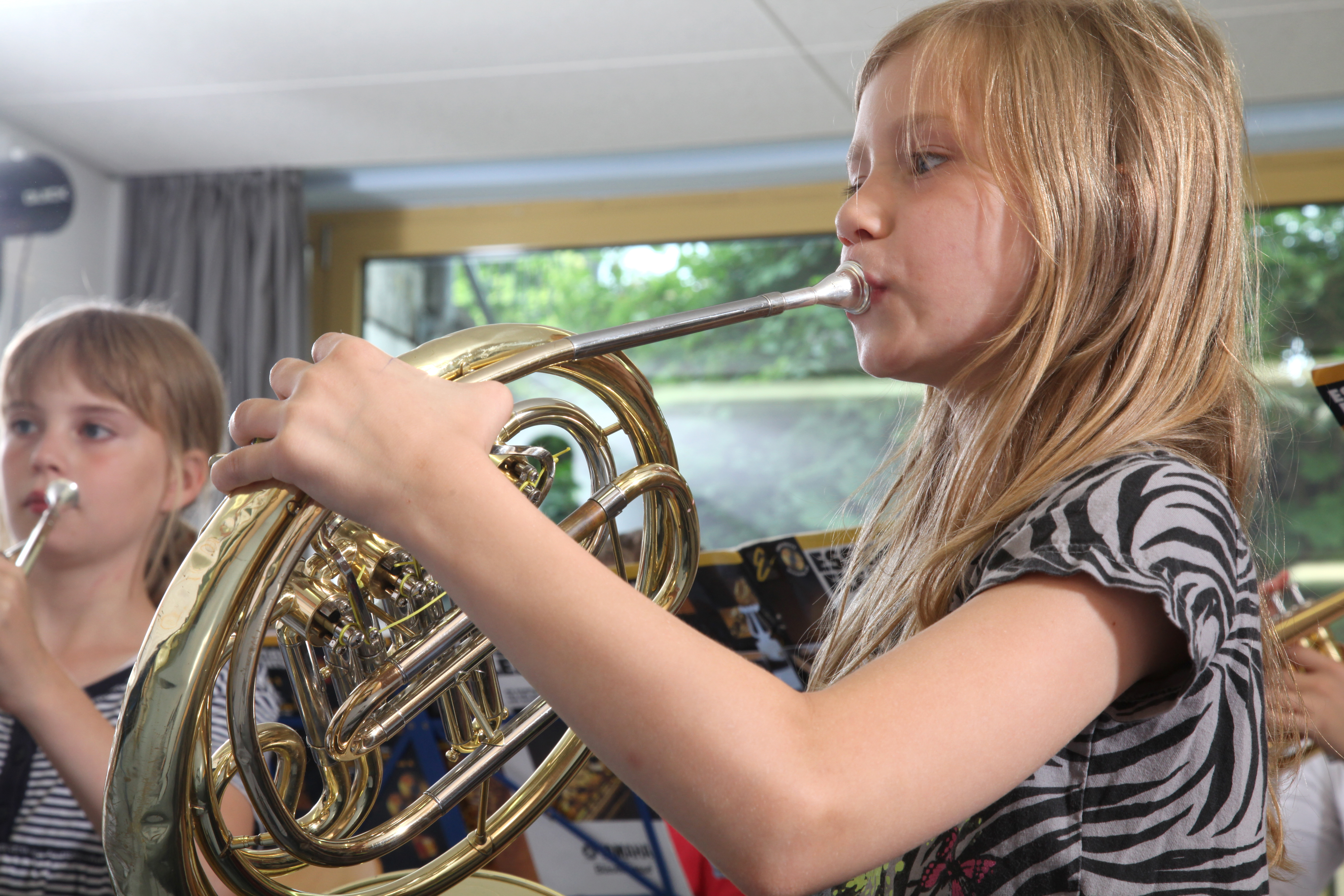 Ein junges Mädchen spielt Horn. 
