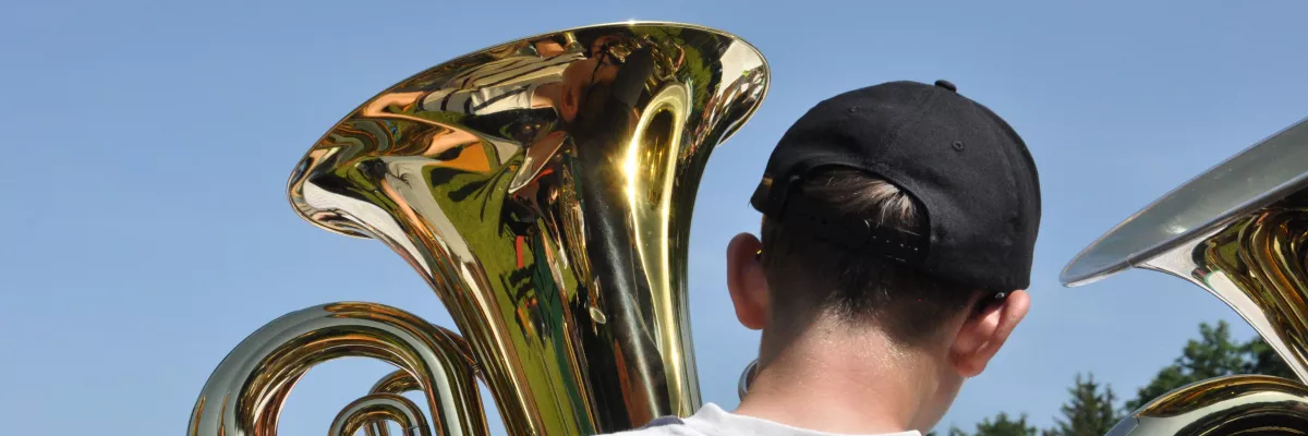Ein Junge spielt Tuba. Im Hintergrund ist blauer Himmel zu sehen.