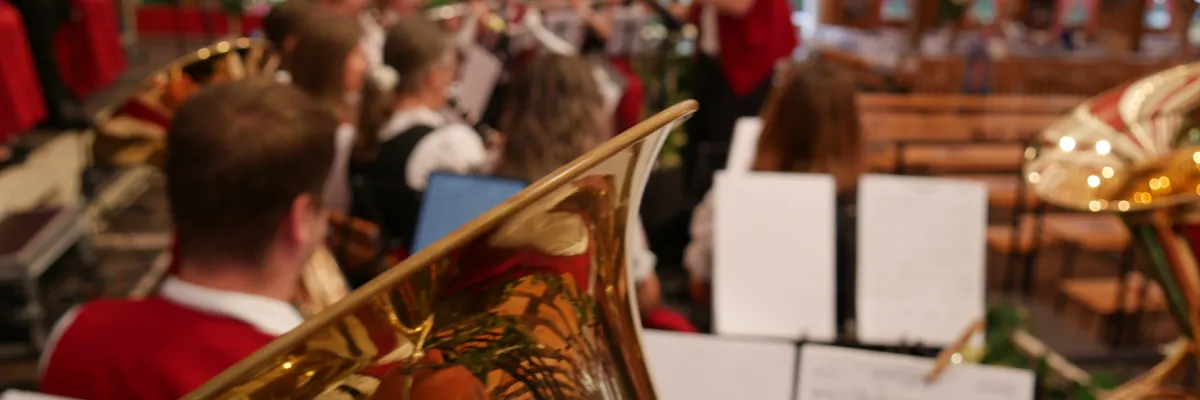 Nahaufnahme eines Tenorhorns. Im Hintergrund ist eine Blaskapelle auf einer Festzelt-Bühne zu sehen.