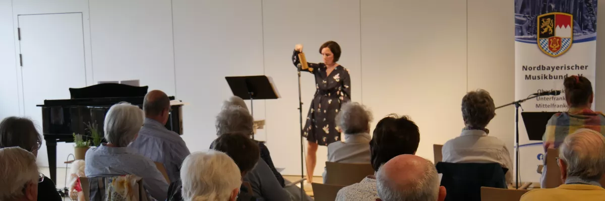 Eine Frau musiziert auf einem Percussion-Instrument vor Senior:innen im Publikum.