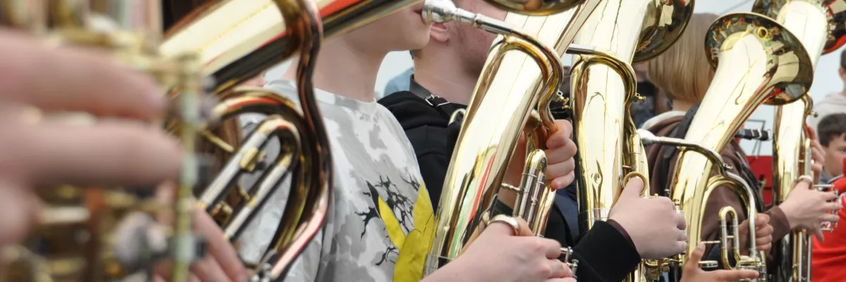 In einem Zelt sitzen einige Kinder nebeneinander und spielen Tenorhorn. 