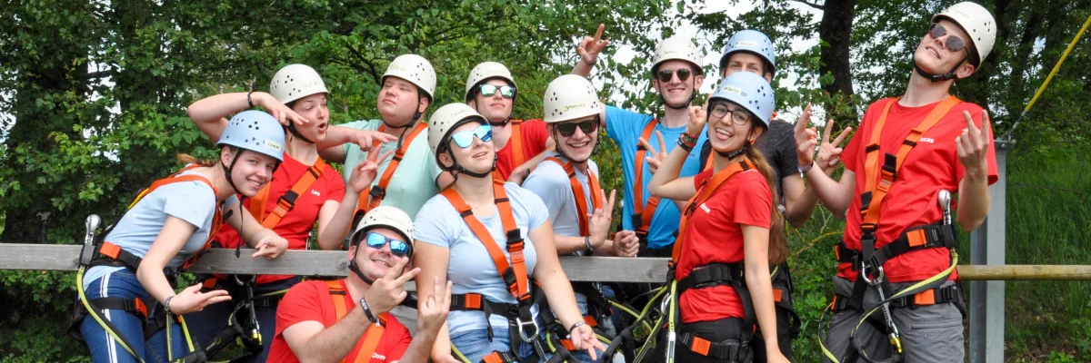 Eine Gruppe Jugendliche mit Kletterausrüstung lacht in die Kamera. 