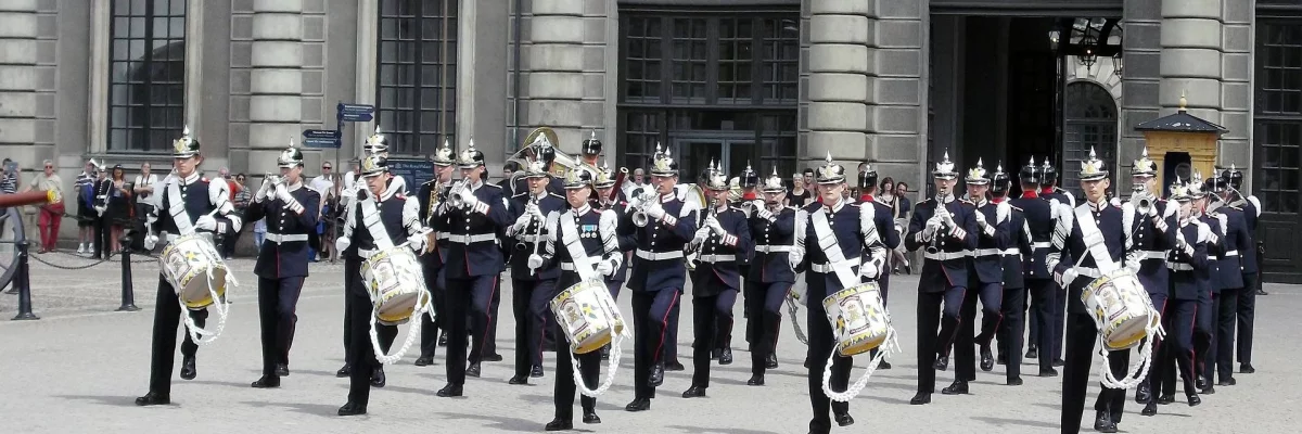 Viele Militärmusiker:innen marschieren in Formation vor einem Schloss und musizieren dabei. 
