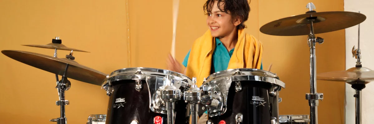 Ein Junge spielt Schlagzeug und lacht. 