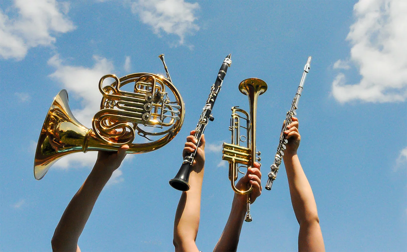 Vier Blasinstrumente werden in den blauen Himmel gehalten. 
