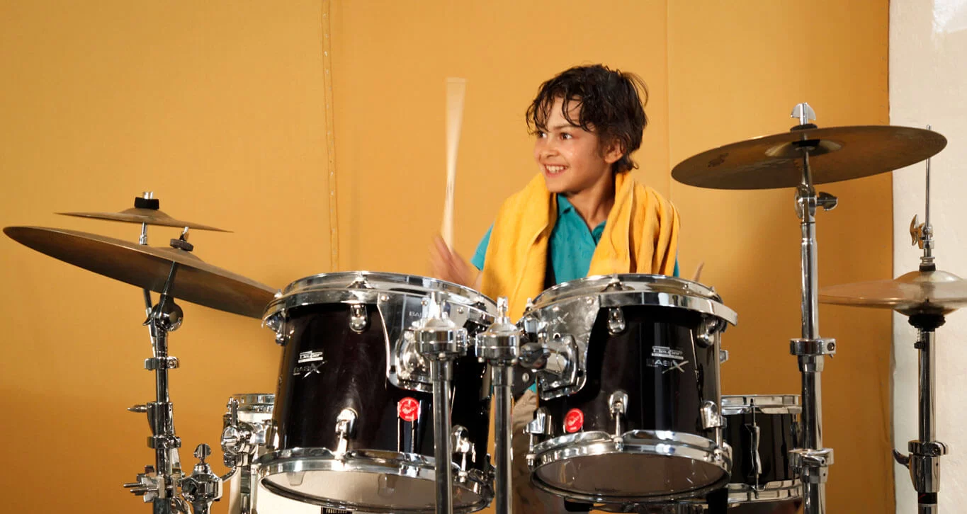 Ein Junge spielt Schlagzeug und lacht dabei.  