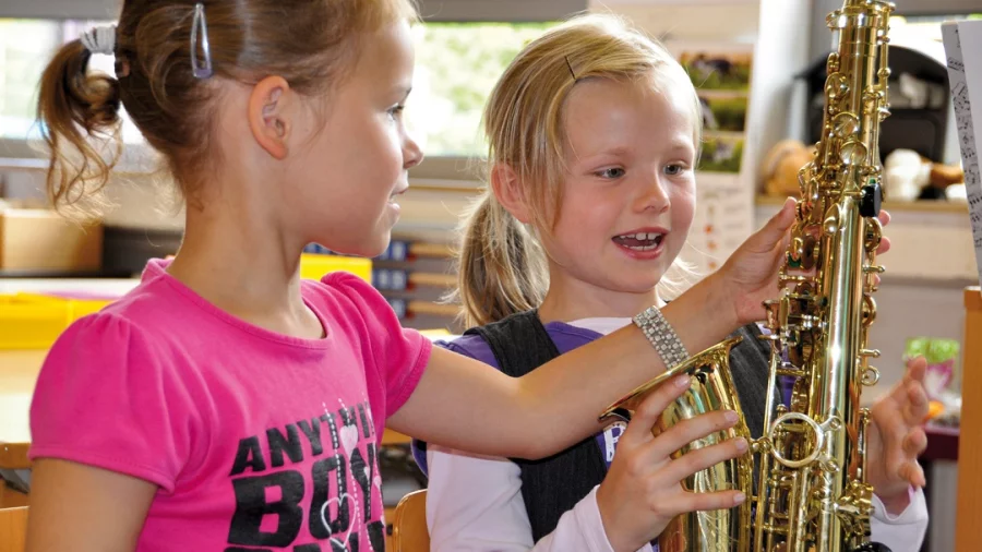 Zwei Mädchen betrachten fasziniert ein Saxophon. 