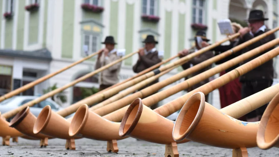 Männer in Tracht spielen Alphorn.