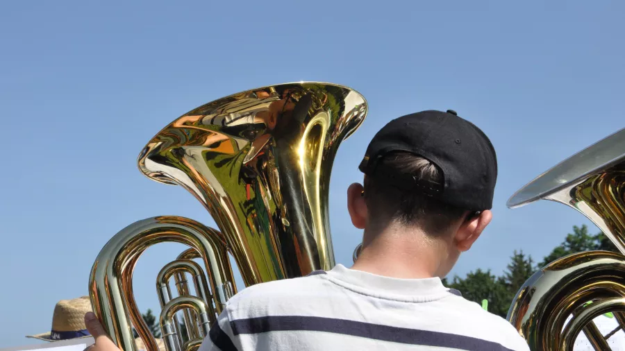 Ein Junge spielt Tuba. Im Hintergrund ist blauer Himmel zu sehen. 