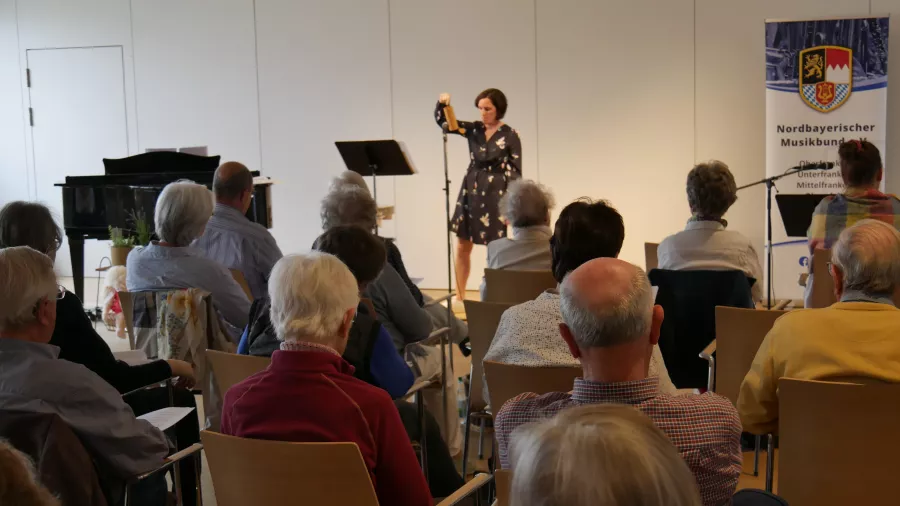 Eine Frau musiziert auf einem Percussion-Instrument vor Senior:innen im Publikum. 