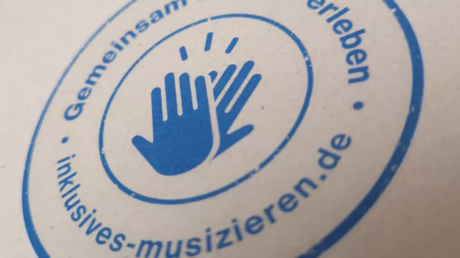 Runder Stempel,  Innen: zwei Hände klatschen ein,  Außen: Text „Gemeinsam Freizeit erleben“ – inklusives-musizieren.de