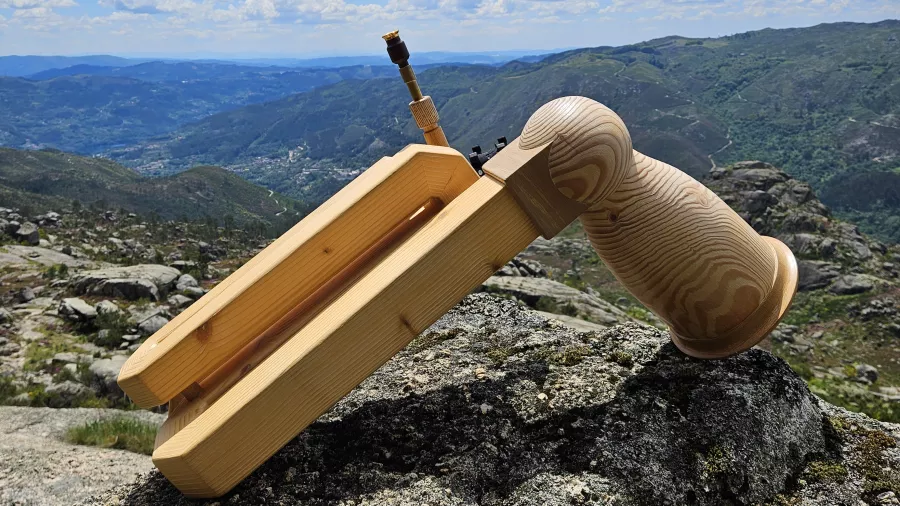 Ein Kompakthorn (Vogelhorn) aus Holz liegt auf Steinboden in der Natur. Im Hintergrund ist ein Bergpanorama zu sehen. 