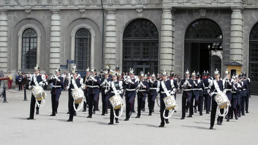 Viele Militärmusiker:innen marschieren in Formation vor einem Schloss und musizieren dabei. 