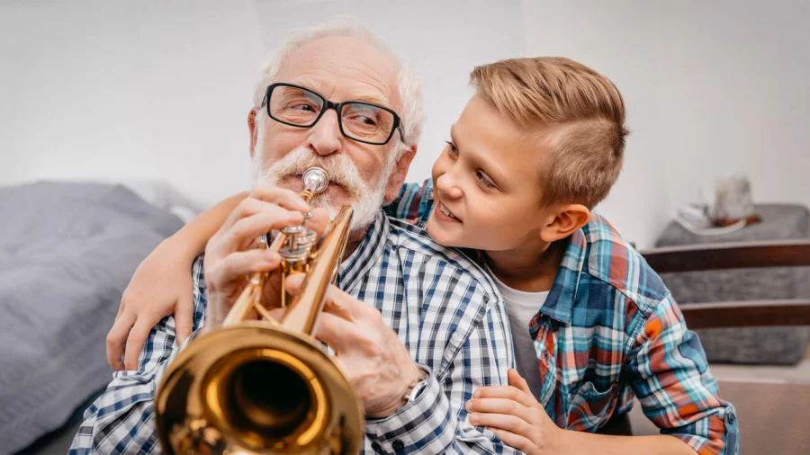 Der Enkel schaut seinem Großvater beim Trompete-Spielen über die Schulter. 