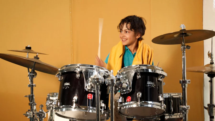 Ein Junge spielt Schlagzeug und lacht dabei.  