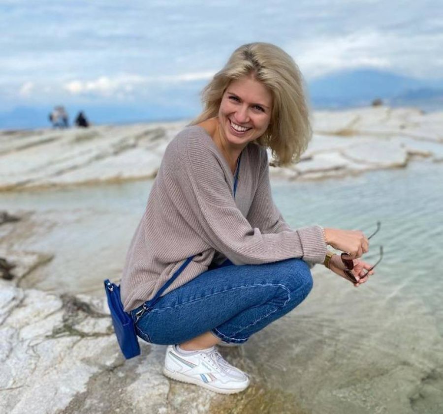 Eine Frau sitzt an einem See und lächelt in die Kamera. 