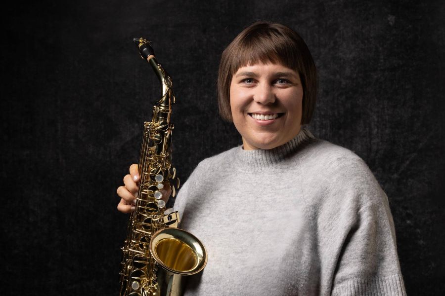 Eine Frau mit einem Saxophon in der Hand lächelt in die Kamera.