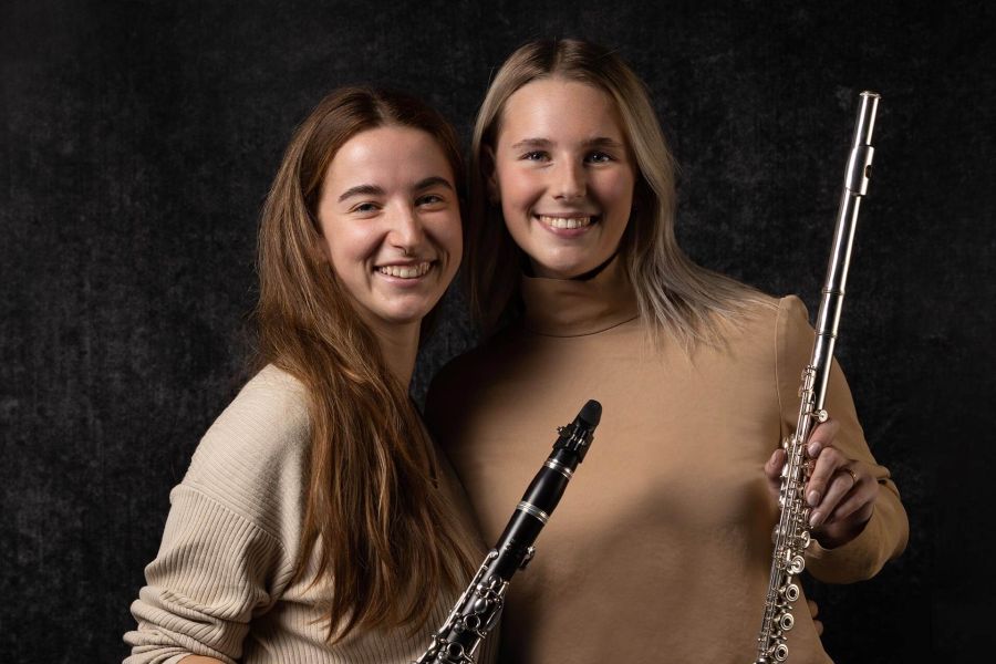 Zwei Frauen mit einer Klarinette und einem Saxophon in der Hand lächeln in die Kamera.